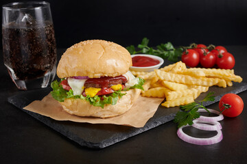 Homemade hamburger or burger with fresh vegetables and cheese lettuce and mayonnaise served, French fries on pieces of brown paper on black stone table . concept of fast food and junk food