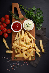 Homemade baked potato fries with mayonnaise, tomato sauce and rosemary on wooden board. tasty...