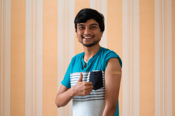 Portrait of an Indian teen giving thumbs up after getting vaccinated and showing bandage on his arm	