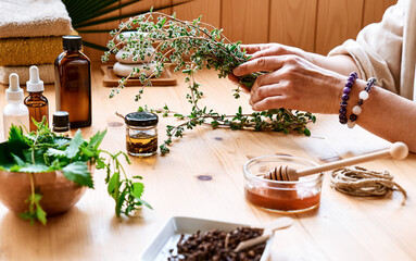 Woman prepares aromatherapy session at the table with essential oil diffuser medical herbs, different types of oils and essences. Aromatherapy and alternative medicine concept. Natural remedies.