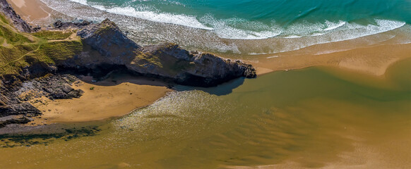 An aerial panorama view above the three cliffs at the Three Cliffs Bay, Gower Peninsula, Swansea, South Wales on a sunny day
