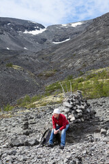 A tourist with a backpack sits on a stone on a mountainside. Rest during the climb to mountain pass. The Khibiny, Russia