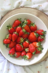 Bowl of fresh strawberries and wooden tray on a bed. Flat lay.