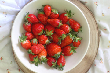 Bowl of fresh strawberries and wooden tray on a bed. Flat lay.
