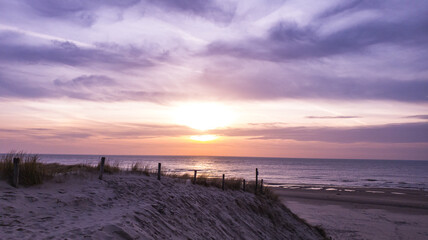 Obraz premium Dramatic sunset over viewing the beach from the dunes, the sunlight is reflected by the sea water and the sun is surrounded by dramatic clouds