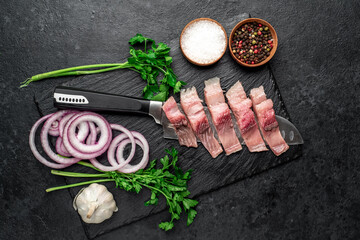 pieces of pickled herring on a knife with onions and herbs on a stone background