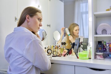 Young woman sitting at make-up table with mirror doing makeup and hairstyle