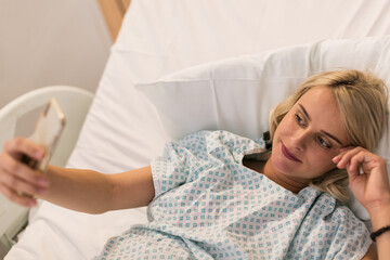 Pregnant woman in maternity hospital lying on bed and taking selfie.