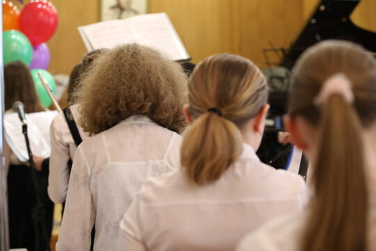 Students girls in white shirts sit behind each other in the classroom in class.Back view.The concept of school music education
