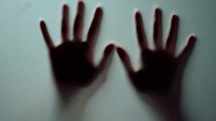 Macro two female hands pressing against glass wall indoors.Blurred hands shadow.