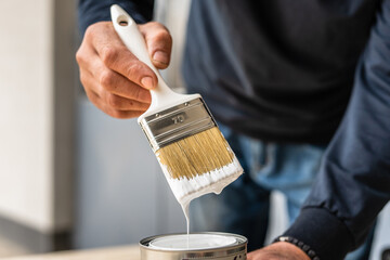 Close up on white paint brush in the hand of unknown man hobby painting and renovation repairing...