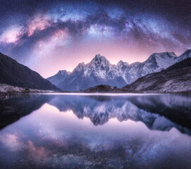 Milky Way over snowy mountains and lake at night. Landscape with snow covered high rocks, purple...