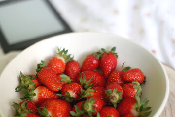 Bowl of strawberries and e-reader on a bed. Selective focus.