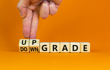 Upgrade or downgrade symbol. Businessman turns wooden cubes, changes words 'downgrade' to 'upgrade'. Beautiful orange table, orange background, copy space. Business and upgrade or downgrade concept.