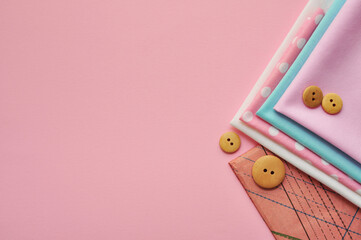 Cotton fabric of different colors, patterns and colored ribbons and wooden buttons on a pink background. Space for text, top view