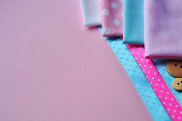 Cotton fabric of different colors, patterns and colored ribbons and wooden buttons on a pink background. Space for text, top view