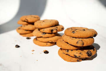 Stacks of chocolate chip cookies with pieces of chocolate in sun light with shadows. Recipe of oatmeal biscuits with chocolate chips. Homemade bakery.