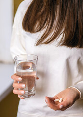 A woman holds a glass of water and two pills in her hands