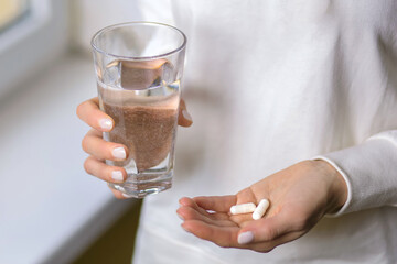 A woman holds a glass of water and two pills in her hands. Young woman treats illness with pills....