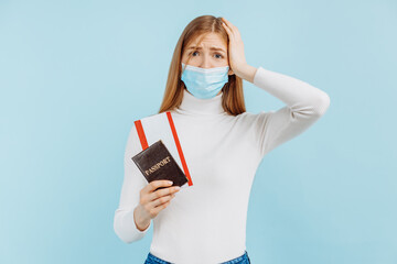 Shocked frightened young woman, in medical mask, holding passport with tickets