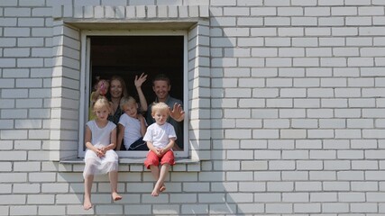 A large family waves their hands and hides from the window of their home.