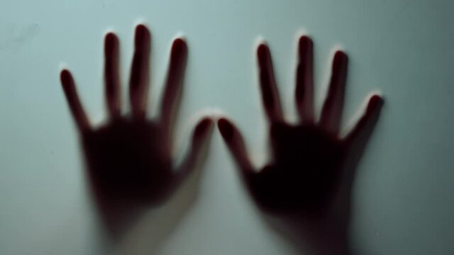 Macro two female hands pressing against glass wall indoors.Blurred hands shadow.