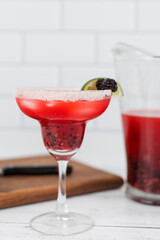A blackberry berry margarita with fresh blackberries and limes in a margarita glass.