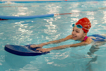 Happy little girl learning to swim with pool board. Sports and entertainment for children. Swimming competition. Healthy lifestyle from childhood.