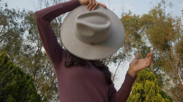 A slow-motion of a young Hispanic woman putting on her fedora hat and throwing it in the air shot in 4K