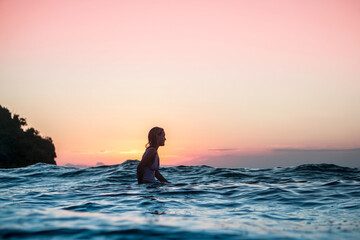 Portrait from the water of surfer girl with beautiful body on surfboard in the ocean at sunset time in Bali