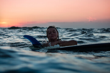 Portrait from the water of surfer girl with beautiful body on surfboard in the ocean at sunset time