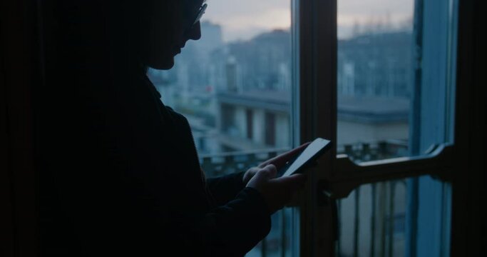 Woman messaging on a phone, Portrait of a millennial with smartphones in his hands against the background of a landscape of a beautiful city in the morning, Female silhouette at sunrise, a dark room