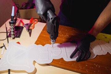 Artisan drilling acrylic board for neon signboard near tools in workshop 