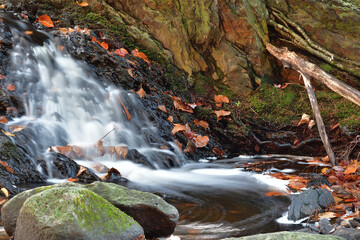 Small waterfall with rocks and dead leafs. Long exposure effect.