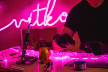 Cropped view of man holding wires of glowing neon near tools in workshop 
