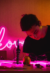 Craftsman holding wires of flex neon while making signboard near tools 