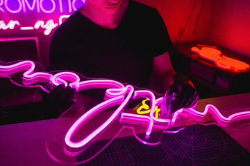 Cropped view of designer cleaning neon signboard with rag in workshop 