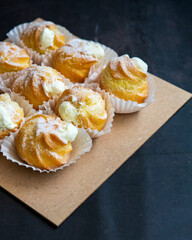 Cream puffs filled with pastry cream and sprinkled with powdered sugar on a dark background.