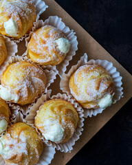 Cream puffs filled with pastry cream and sprinkled with powdered sugar on a dark background.