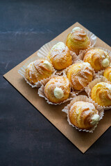 Cream puffs filled with pastry cream and sprinkled with powdered sugar on a dark background.