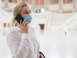 Stylish mature lady in protective face mask speaking on smartphone in art museum