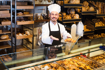 Man is offering fresh tasty croissant in bakery.