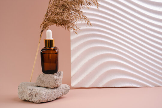 The bottle of Essence is on the pedistal. Lotion on a beige background. Cosmetics for skin health. Aromo Oil. Serums with vitamin C. Unisex cosmetics. Mockup. 