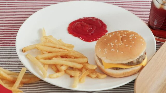 Close-ups, selective focus on ketchup in a white dish on tablecloths that are poured out of red bottles for junk food snacks, including takeaway hamburgers, french fries, snacks, and cola. 