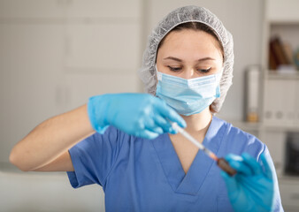 Fototapeta na wymiar Girl nurse in mask holding syringe for injection in modern clinic