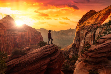 Adventurous Woman at the edge of a cliff is looking at a beautiful landscape view in the Canyon. Sunset Sky Art Render. Taken in Zion National Park, Utah, United States. - obrazy, fototapety, plakaty
