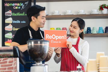 Portrait of man and woman waitress standing at her coffee shop gate with showing closed signboard