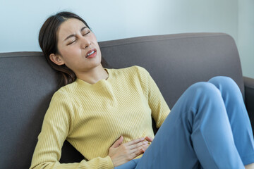 Flatulence asian young woman, girl lying, sitting in stomach ache, suffer from food poisoning, abdominal pain and colon problem, gastritis or diarrhoea.Patient belly, abdomen or inflammation, concept.