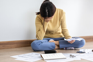 Fototapeta premium Front view owe asian woman, female sitting on floor home, stressed and confused by calculate expense from invoice or bill, have no money to pay, mortgage or loan. Debt, bankruptcy or bankrupt concept.