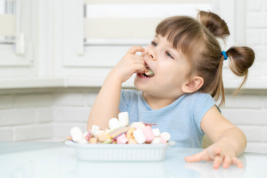 cute European female child smiling, happily eating candy, with appetite. sugar abuse, unhealthy sweet food concept, child candy addiction and child dental care